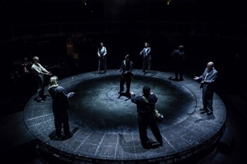  The full company stand in a lit ring on the edge of the circular stage. In the centre of the stage stands Kay Langrish (Jodie McNee) in a soft edged spotlight. 