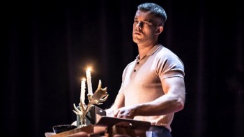  Bill (Russell Tovey) carries a tray with a bowl, radio and antler shaped candelabra holding two lit candles. He's wearing a beige 60s style polo shirt. 