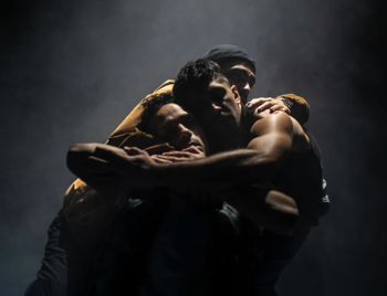 The cast embracing one another surrounded by light in a thick haze.