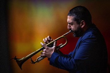Ibrahim Maalouf playing the trumpet against an orange projection.