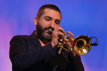 Ibrahim Maalouf playing the trumpet against a blue and pink projection background.